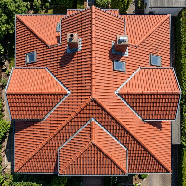 Drohnenaufnahme eines roten Ziegeldaches von oben mit Dachfenstern und Schornstein
